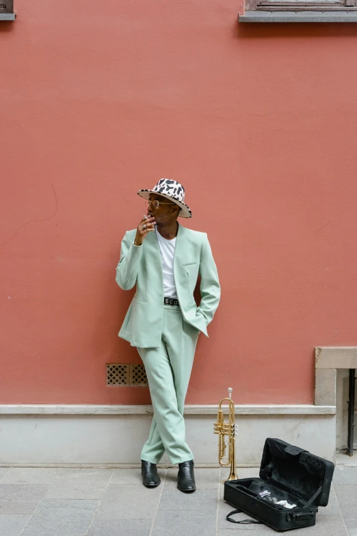 a man in a green suit leaning against a pink wall, by Nina Hamnett, pexels contest winner, renaissance, imaan hammam, wearing a travel hat, trumpet, pastel green