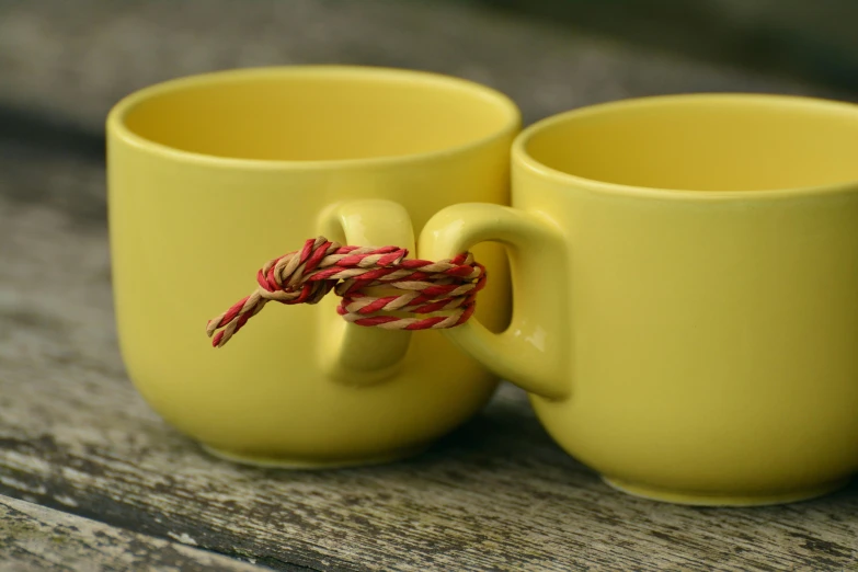 a couple of yellow cups sitting on top of a wooden table, inspired by Sarah Lucas, unsplash, rope bondage, holding each other, red yellow, at the waterside