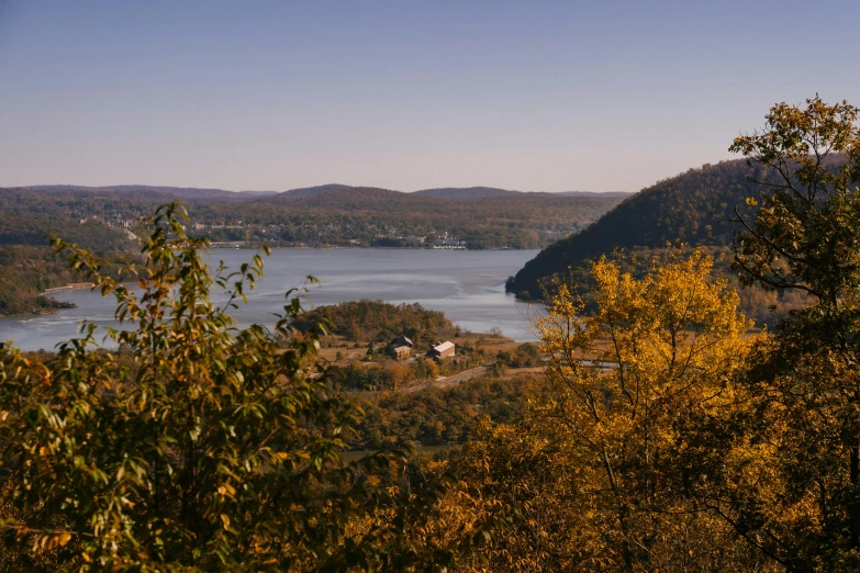 a large body of water surrounded by trees, pexels, hudson river school, distant town in valley and hills, shades of gold display naturally, slide show, high cliff