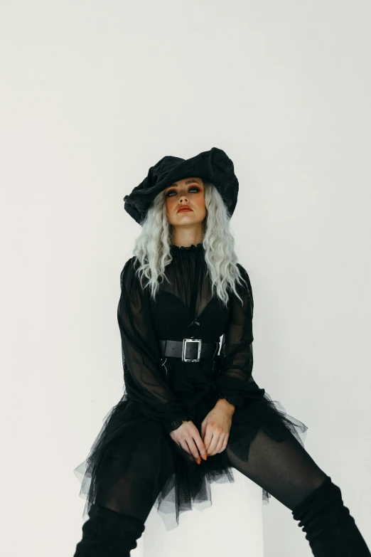 a woman sitting on top of a white box, an album cover, trending on pexels, rococo, wearing black witch hat, curly white hair, black dress with belt, portrait featured on unsplash