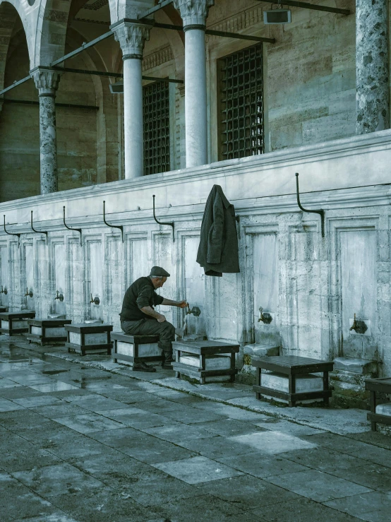 a man sitting on a bench in front of a building, a colorized photo, by Elsa Bleda, pexels contest winner, renaissance, tiled fountains, the fall of constantinople, white marble interior photograph, ( ( theatrical ) )