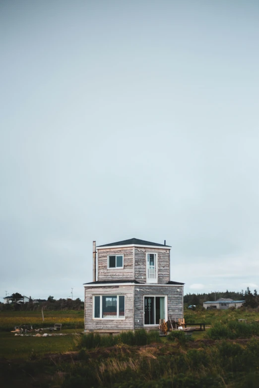 a small house sitting on top of a lush green field, a portrait, by Jessie Algie, unsplash, minimalism, tall thin build, coastal, tiny house, grey sky