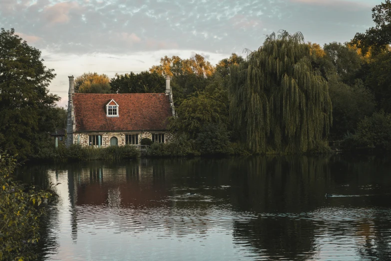 a house sitting next to a body of water, by Bertram Brooker, pexels contest winner, arts and crafts movement, thames river, crystal lake, guardian of the holy lake, parks and lakes