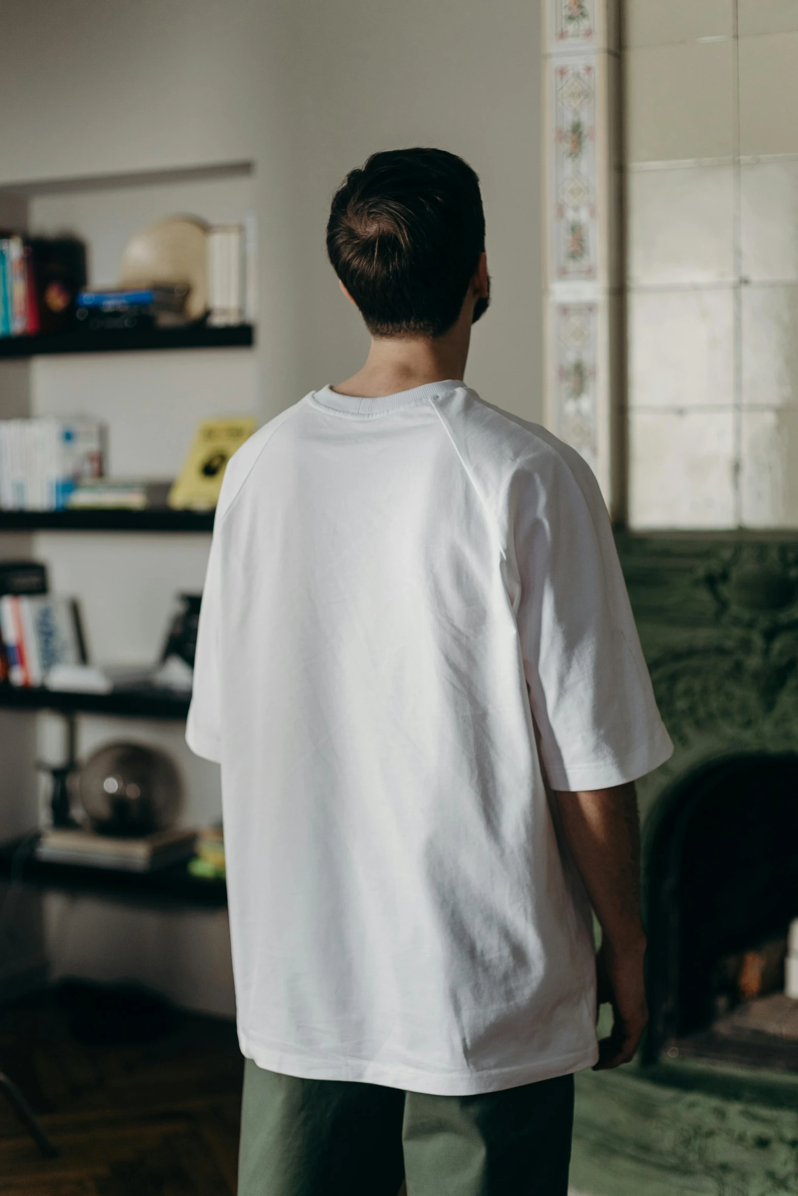 a man standing in front of a fireplace in a living room, by Tobias Stimmer, featured on reddit, white t-shirt, 3 / 4 view from back, sport t-shirt, the last portrait of mac miller