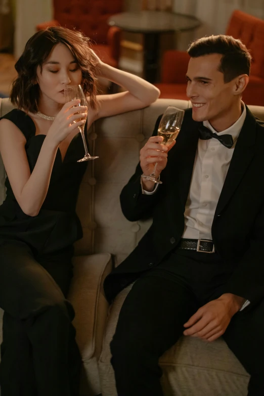 a man and a woman sitting on a couch holding wine glasses, tailored clothing, bubbly, nights, college