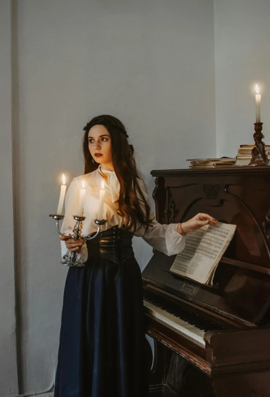 a woman standing next to a piano holding a lit candle, an album cover, inspired by Vasily Perov, pexels contest winner, baroque, victorian gothic lolita fashion, performing a music video, white candles, portrait of a young witch