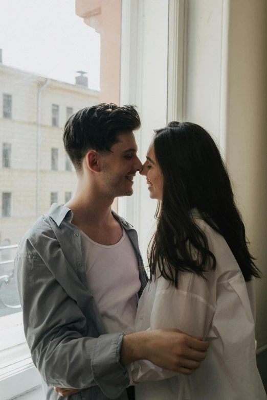 a man and a woman standing in front of a window, by Cosmo Alexander, pexels contest winner, flirting smiling, killian eng, brunettes, instagram post