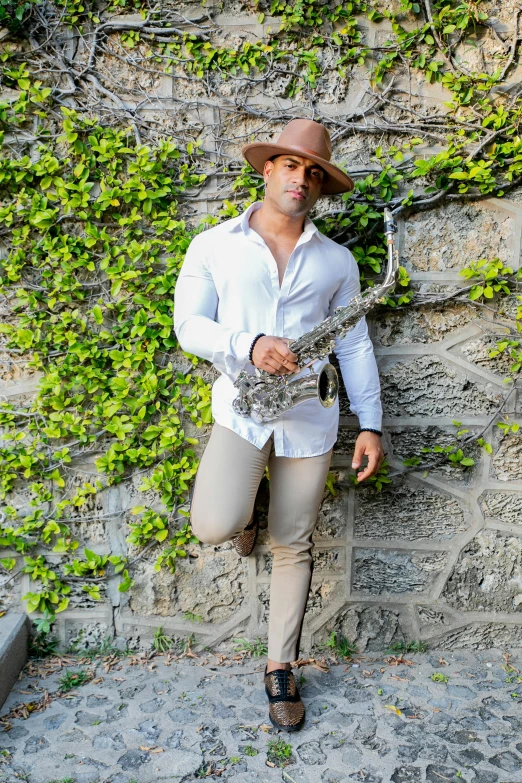 a man standing in front of a stone wall, an album cover, inspired by Hugo Sánchez Bonilla, pexels contest winner, renaissance, saxophone, white suit and hat, in a tree, model posing