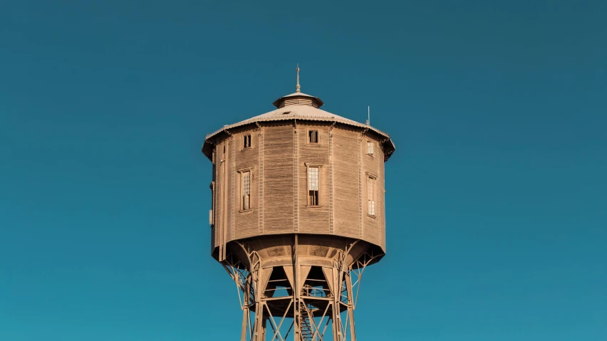 a wooden water tower against a blue sky, unsplash, renaissance, wes anderson film, old color photograph, brown, blue