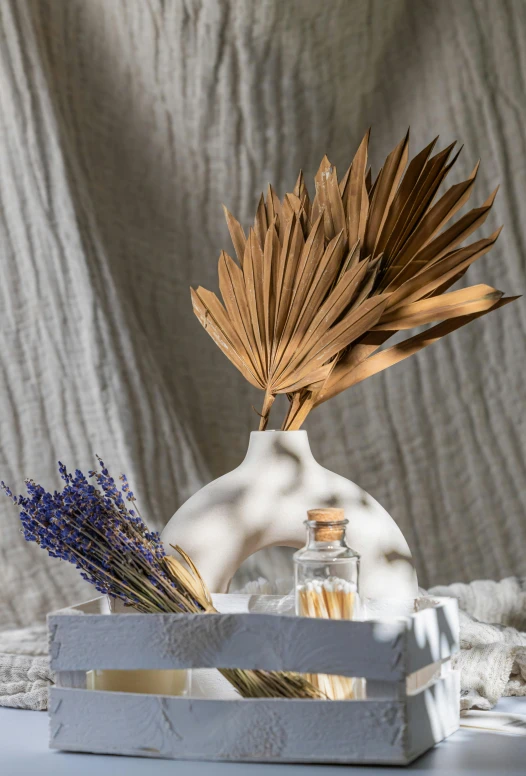 a white vase sitting on top of a table, an abstract sculpture, inspired by Andrea del Verrocchio, palm leaves on the beach, dried herbs, shades of gold display naturally, professional product photo