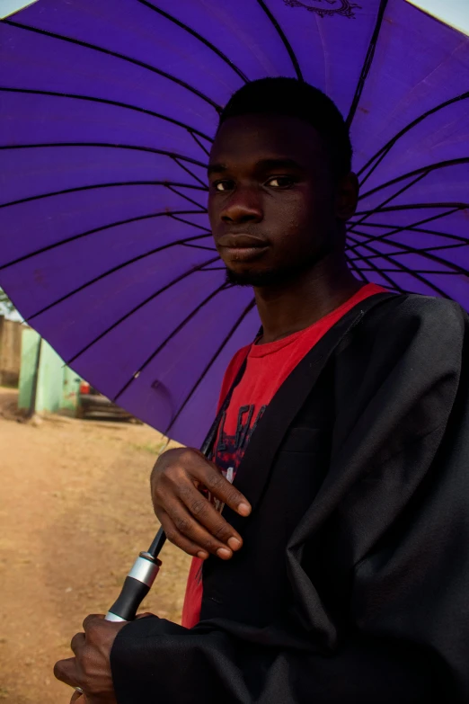 a man holding a purple umbrella on a dirt road, by Ingrida Kadaka, 2 3 years old, looking serious, ((purple)), ( ( theatrical ) )