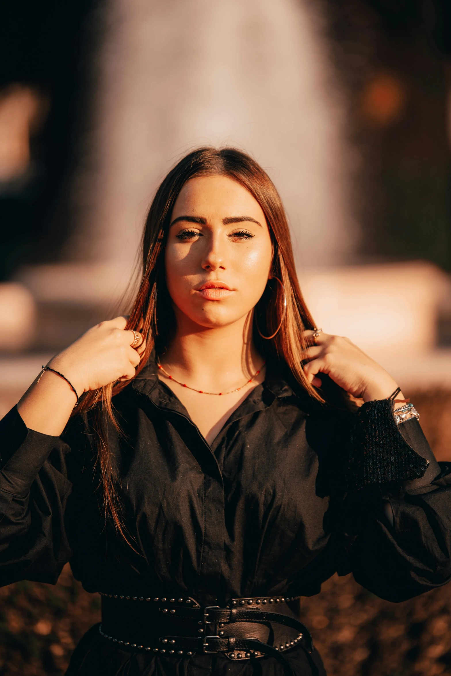 a woman standing in front of a fountain, an album cover, by Julia Pishtar, trending on pexels, wearing a black shirt, jewelry, young middle eastern woman, cropped shirt with jacket