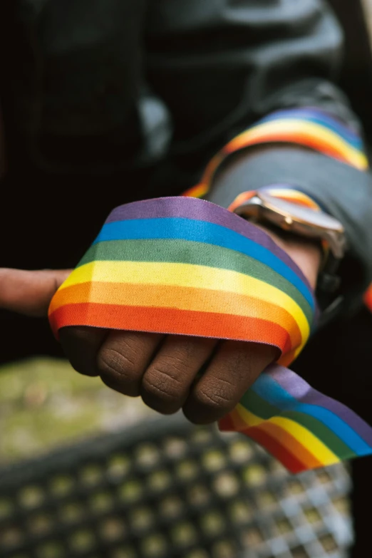 a close up of a person holding a rainbow ribbon, inspired by Okuda Gensō, unsplash, police tape, gauntlets, brown, 🚿🗝📝