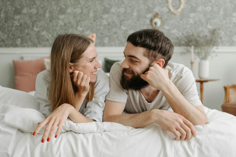 a man and woman laying in bed next to each other, pexels contest winner, curled beard, smiling at each other, promo image, profile image