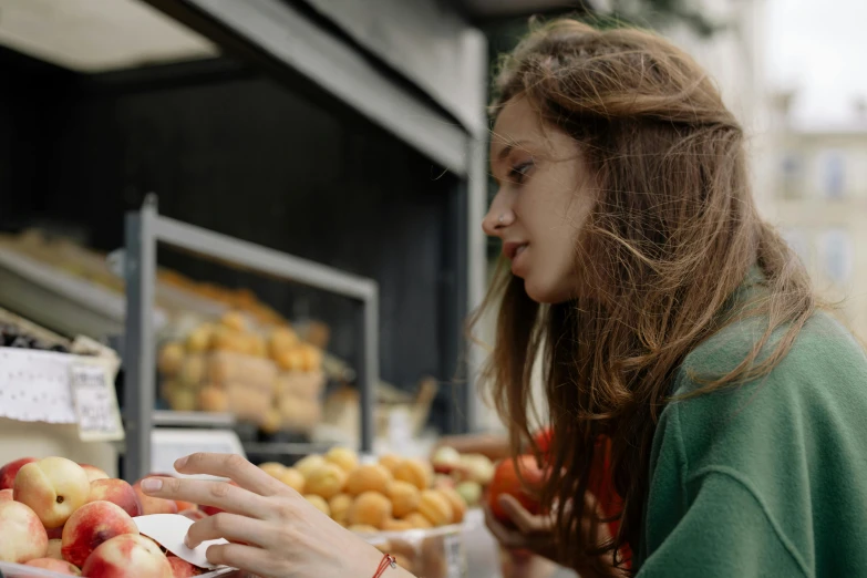a woman standing in front of a display of apples, by Emma Andijewska, pexels contest winner, eating garlic bread, in a sidewalk cafe, girl with brown hair, profile image