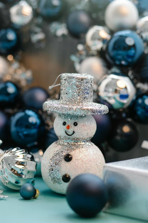 a snowman sitting on top of a table next to christmas ornaments, blue and silver, zoomed in, thumbnail, navy