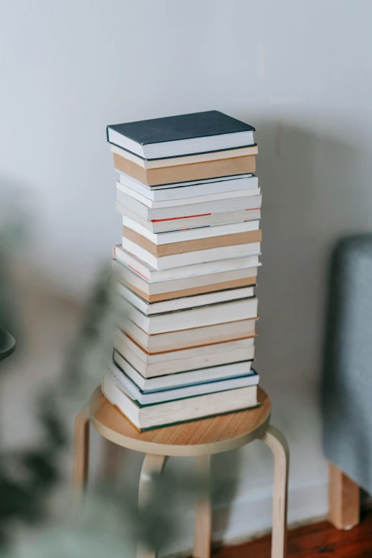 a stack of books sitting on top of a wooden stool, tall towers, on a white table, perfect readability, curated collection