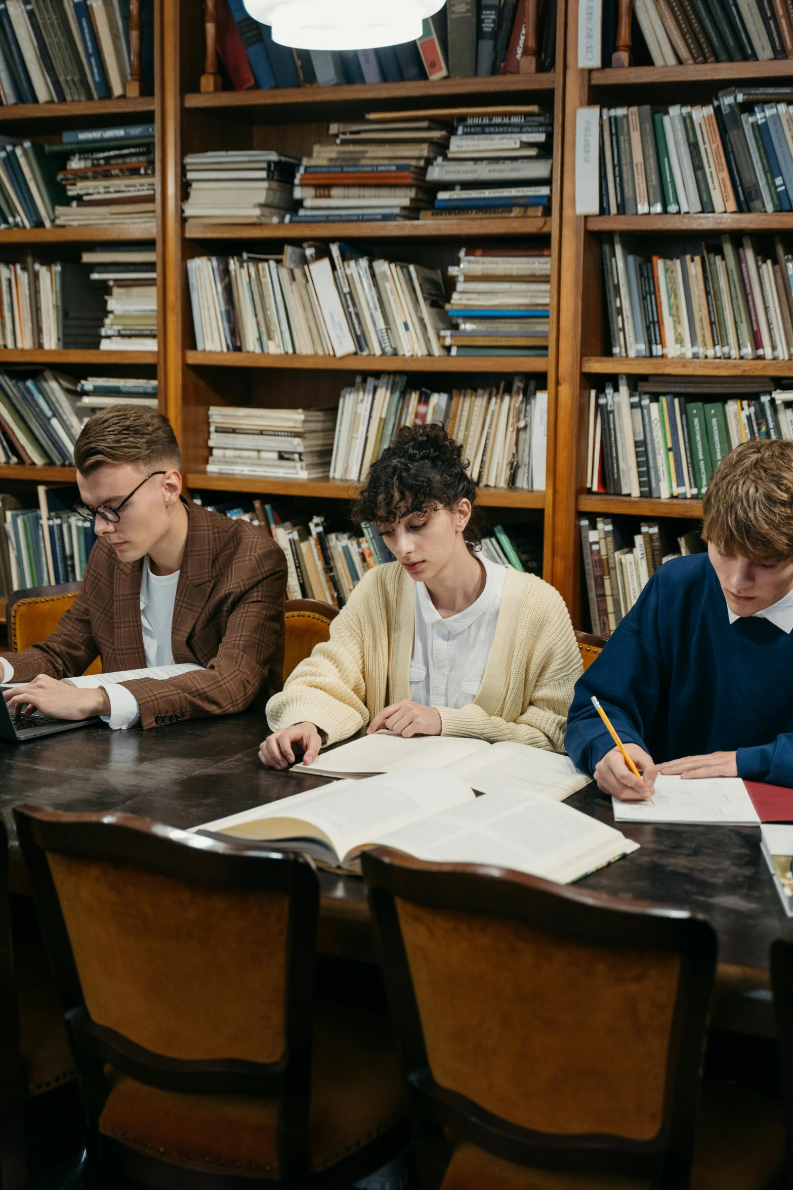a group of people sitting around a table in a library, unsplash, academic art, cute boys, russian academicism, ignant, non-binary