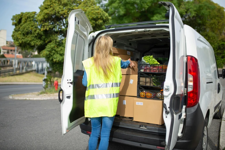 a woman loading boxes into the back of a van, a picture, shutterstock, square, wearing hi vis clothing, 6k, ready to eat