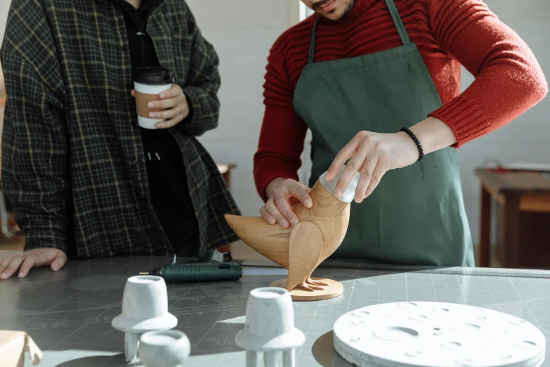 a couple of people standing around a table, a surrealist sculpture, inspired by Hendrik Gerritsz Pot, unsplash, process art, holding a white duck, clay material, in the shape of a cinnamon roll, geometric