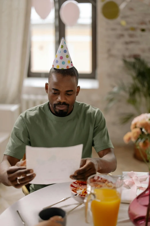 a man in a party hat sitting at a table, mkbhd, reading for a party, caring fatherly wide forehead, abcdefghijklmnopqrstuvwxyz