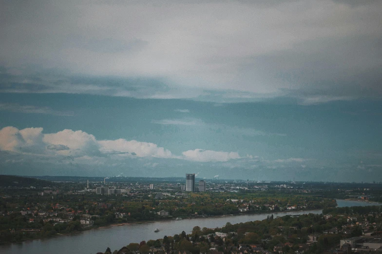 a view of a city from the top of a hill, by Emma Andijewska, pexels contest winner, thames river, grainy footage, germany. wide shot, clouds around