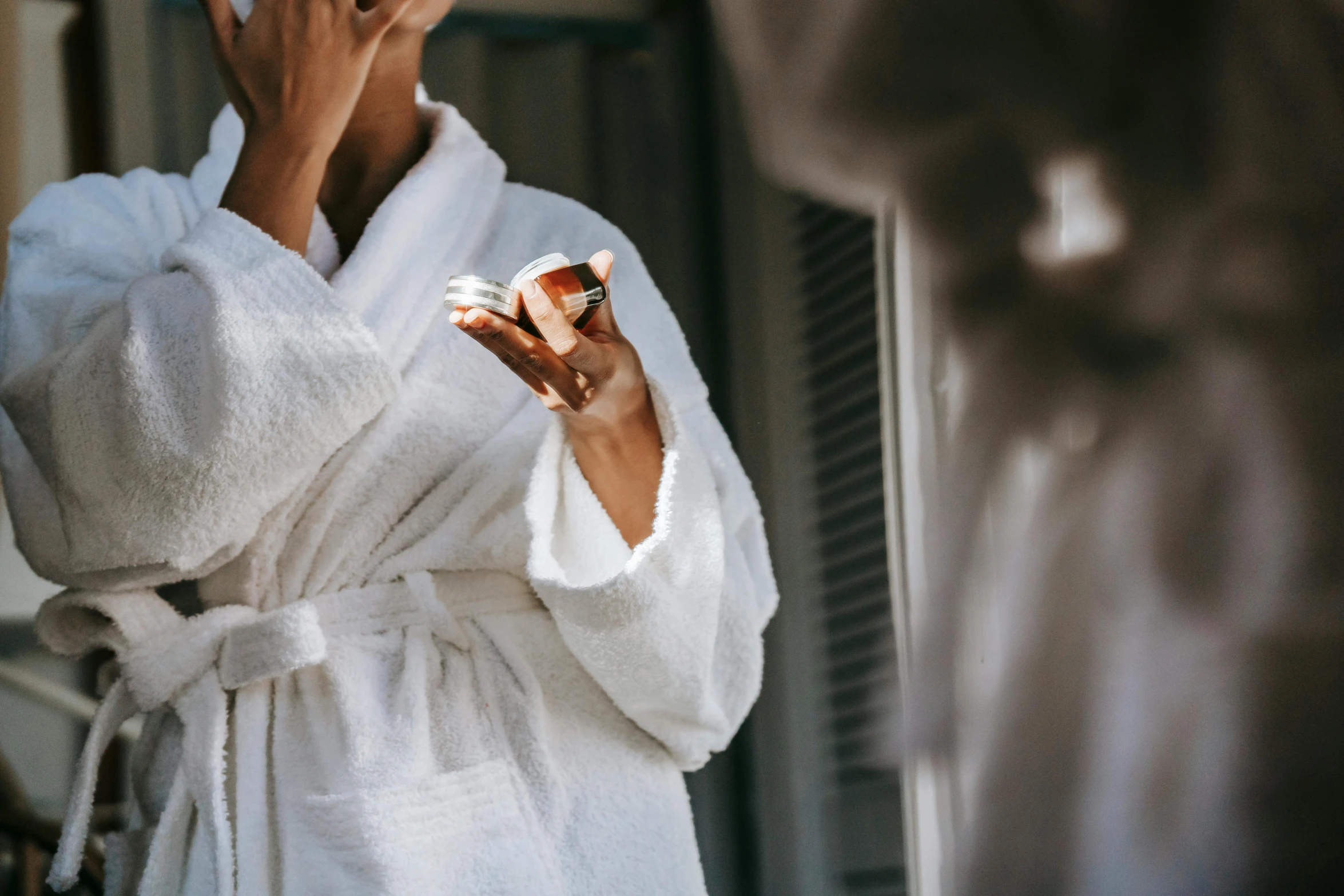 a woman standing in front of a mirror brushing her teeth, pexels contest winner, happening, wearing long white robe, carrying a bottle of perfume, exterior shot, spa