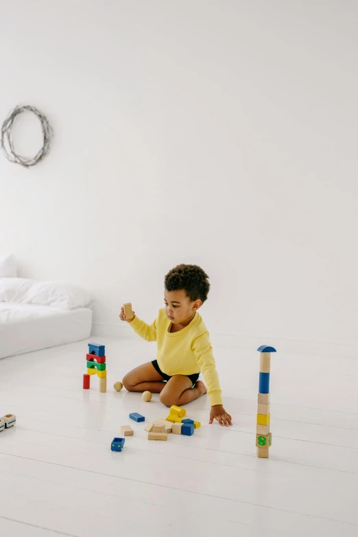 a baby sitting on the floor playing with blocks, pexels contest winner, minimalism, in a white room, yellow and blue, promo image, diverse ages