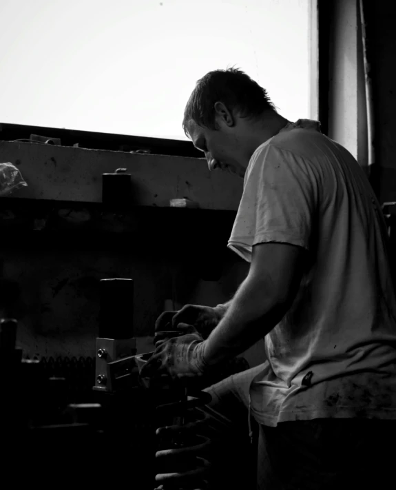 a black and white photo of a man working on a machine, by Rihard Jakopič, unsplash, arbeitsrat für kunst, woodfired, profile pic, sittin, carving