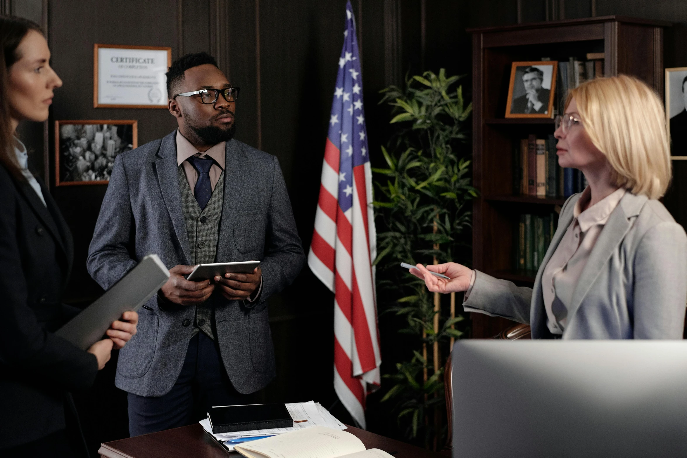 a group of people standing around a desk, patriotism, defense attorney, background image, ( ( theatrical ) )