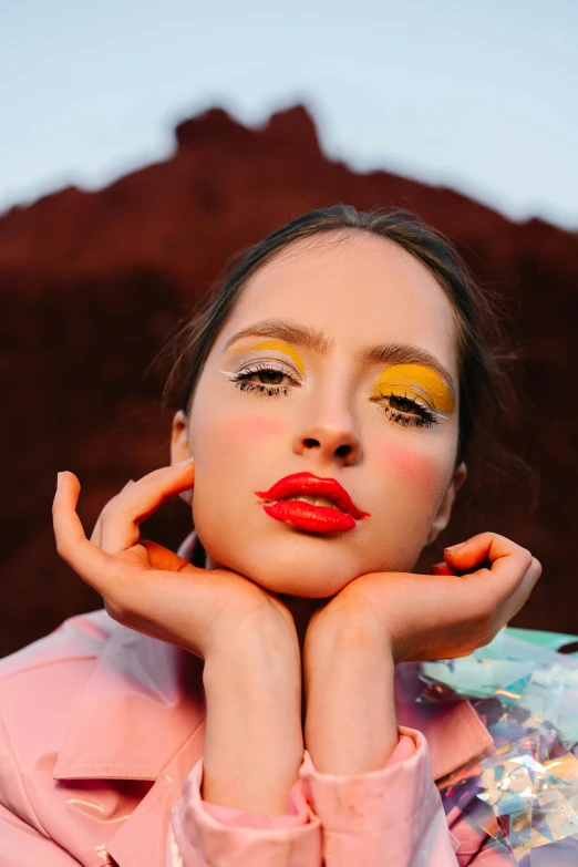 a woman is posing with her hands on her face, an album cover, by Julia Pishtar, trending on pexels, yellow makeup, bright red desert sands, coral lipstick, pastels