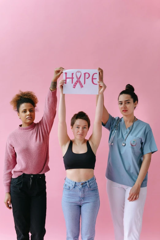 three women holding up a sign that says hope, by Olivia Peguero, trending on pexels, antipodeans, ((pink)), medical image, woman posing, college