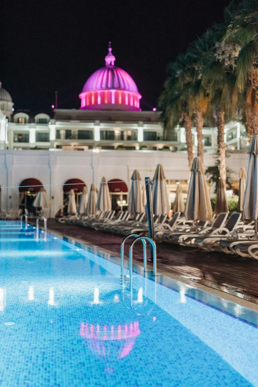 an outdoor swimming pool with lounge chairs and umbrellas, by Julia Pishtar, art nouveau, set in observatory at night, jerez, in a beachfront environment, dome