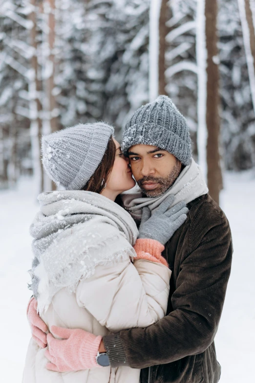 a man and woman standing next to each other in the snow, pexels contest winner, knitted hat, holding each other, mixed race, an elegant