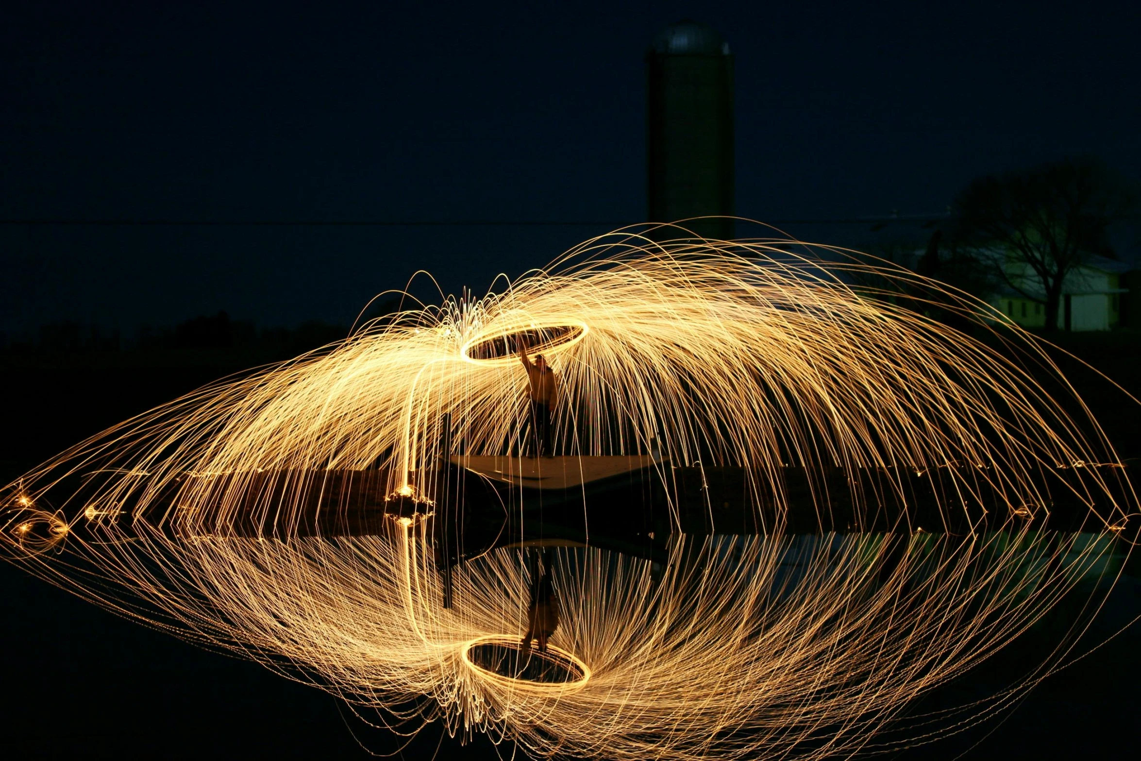 a man standing next to a body of water at night, spinning, large electrical gold sparks, outdoor photo, intricate sharp focus