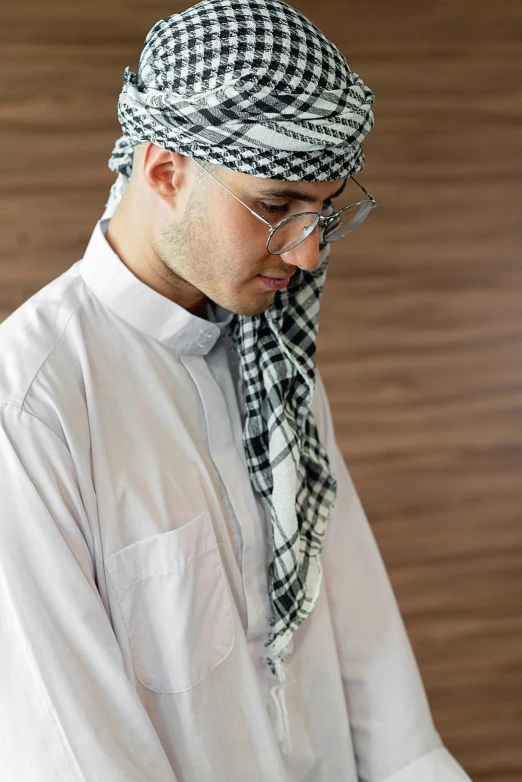 a man in a white shirt and black and white checkered scarf, inspired by Fathi Hassan, trending on pexels, tight wrinkled cloath, dressed thobe, contemplating, jewish young man with glasses