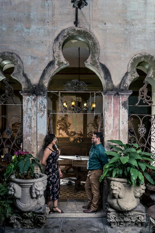 a man and a woman standing in front of a building, inspired by Luis Paret y Alcazar, art nouveau, archways made of lush greenery, marble room, cuban setting, ornate dining hall