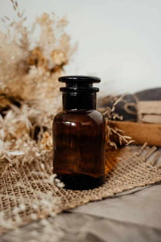 a brown glass bottle sitting on top of a table, by Jessie Algie, unsplash, apothecary, lush flora, black, sustainable materials