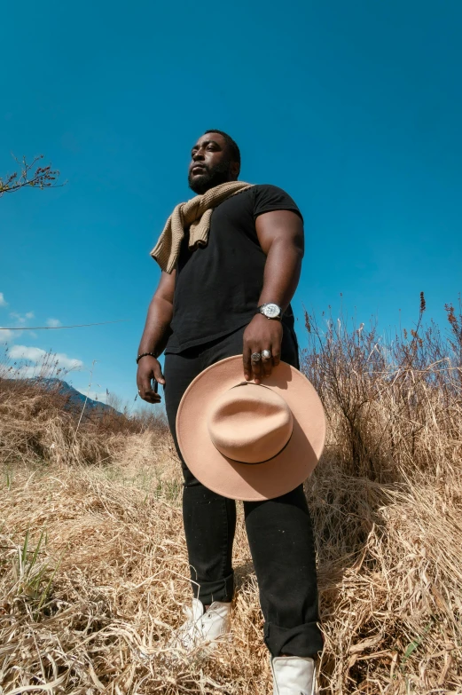 a man standing in a field with a hat, an album cover, pexels contest winner, man is with black skin, beefy, influencer, thicc