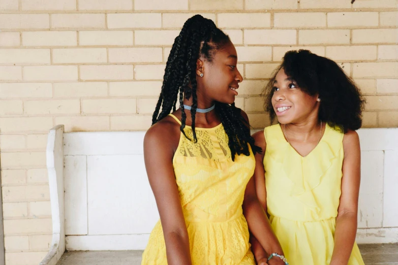 a couple of women standing next to each other, by Carey Morris, pexels, happening, black teenage girl, wearing a yellow dress, family friendly, schools