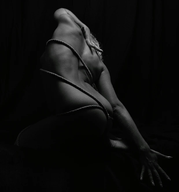 a black and white photo of a naked woman, an album cover, inspired by Hans Bellmer, unsplash, figurative art, rope bondage, back lit, sitting pose, dark dance photography aesthetic