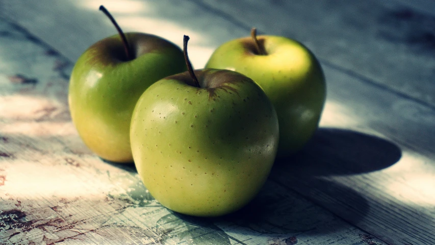 three green apples sitting on top of a wooden table, inspired by Elsa Bleda, unsplash, fan favorite, snacks, vintage photo, background image