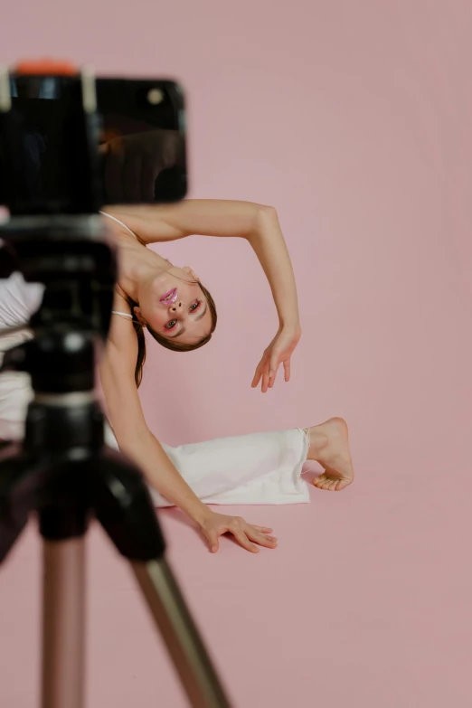 a woman sitting on top of a tripod next to a camera, inspired by Elizabeth Polunin, trending on pexels, video art, ballet style pose, photoshoot for skincare brand, rectangle, in an action pose