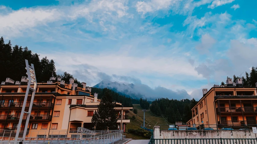 a couple of buildings sitting next to each other, by Alexis Grimou, pexels contest winner, : psychedelic ski resort, swirly clouds in the background, late summer evening, thumbnail