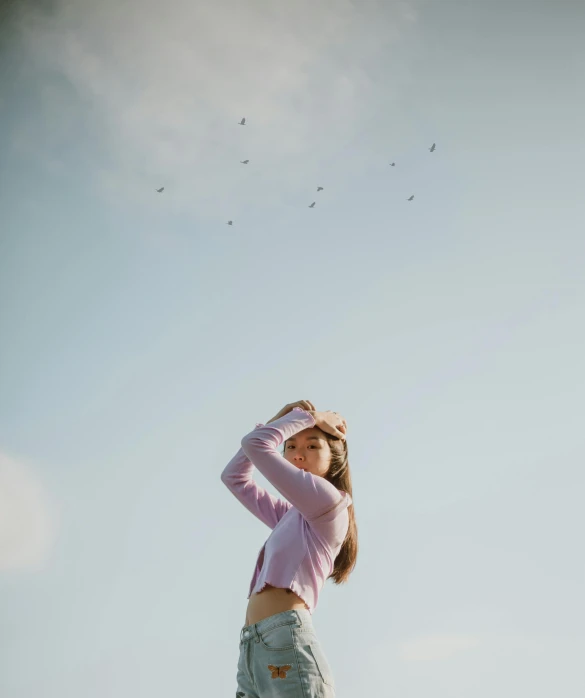 a woman standing on top of a lush green field, an album cover, by Attila Meszlenyi, pexels contest winner, throwing cards in the air, wearing a pastel pink hoodie, birds on sky, minimalist photo