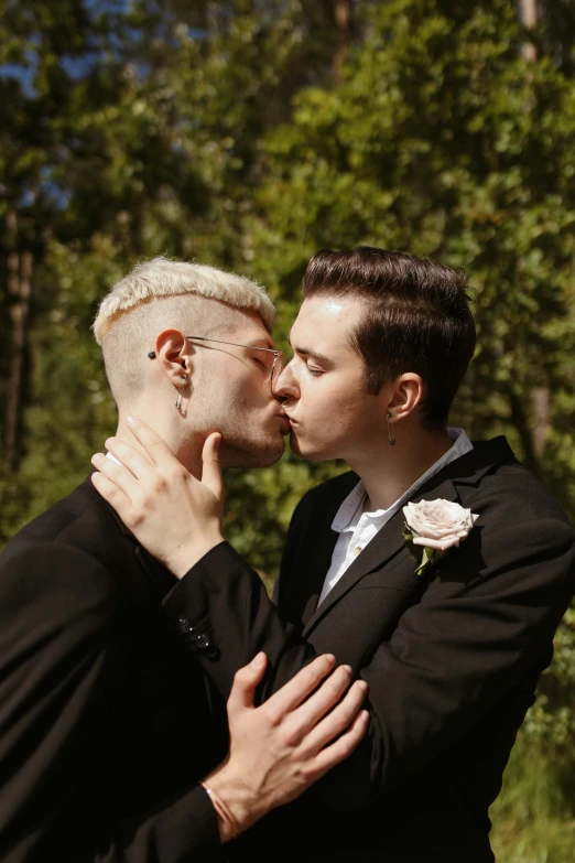 a couple of men standing next to each other, kissing, albino hair, lush surroundings, zachary corzine