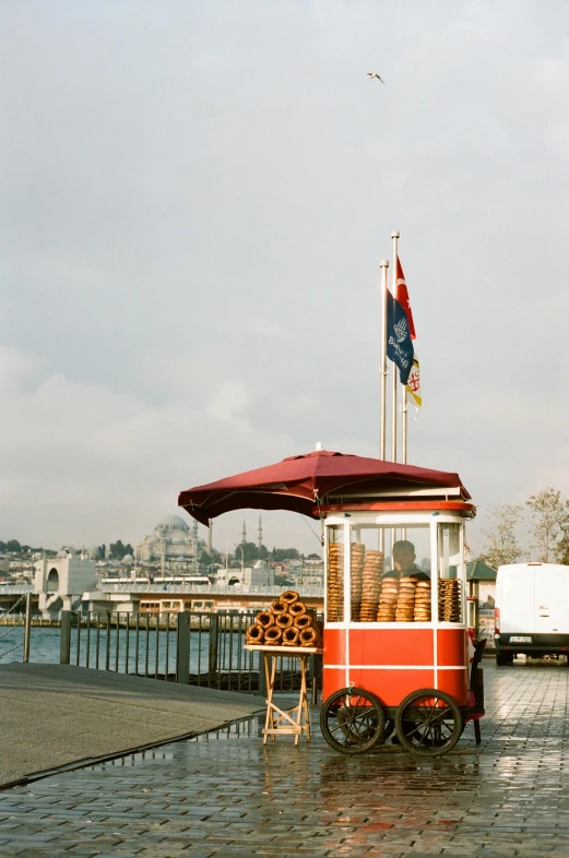 a red and white cart sitting next to a body of water, pastries, docked at harbor, medium format. soft light, donut