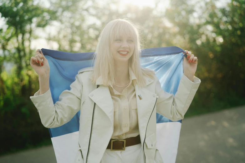 a woman is holding a blue and white flag, an album cover, by Attila Meszlenyi, pexels contest winner, symbolism, albino hair, excited russians, belle delphine, capital of estonia
