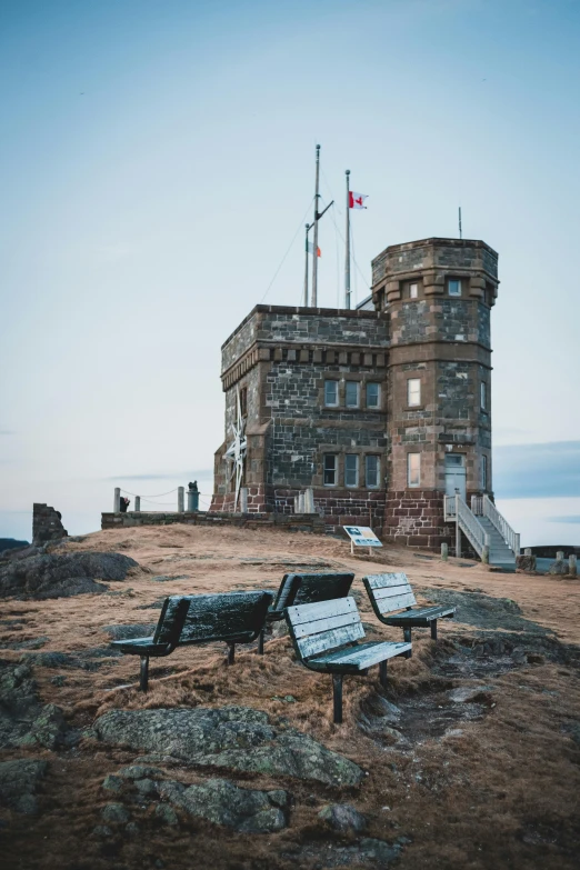 a couple of benches sitting on top of a hill, a colorized photo, pexels contest winner, hudson river school, giant imposing steampunk tower, seaside victorian building, standing on rocky ground, military outpost