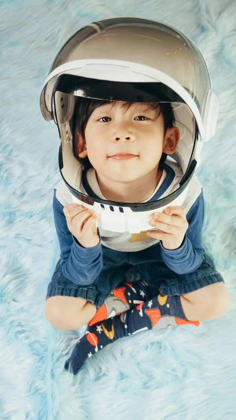 a close up of a child wearing a helmet, pexels contest winner, shin hanga, on a spaceship, smiling down from above, sitting on the floor, thumbnail